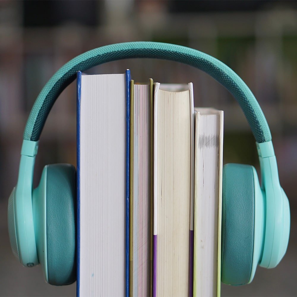 Des livres alignés verticalement entourés d’un casque audio turquoise, illustrant le concept de livre audio et l’accessibilité à la lecture via l’écoute.